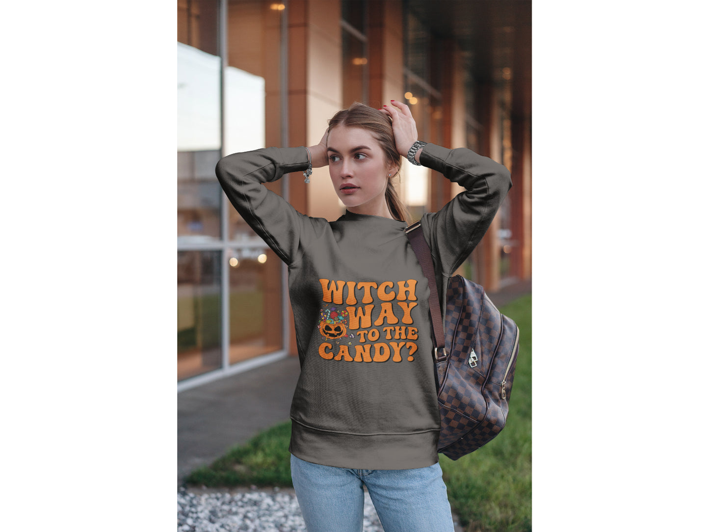 A woman wears a dark gray sweatshirt with "Witch Way to the Candy?" in orange text.