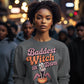A woman wears a dark gray sweatshirt with "Baddest Witch in Town" text and a witch graphic.