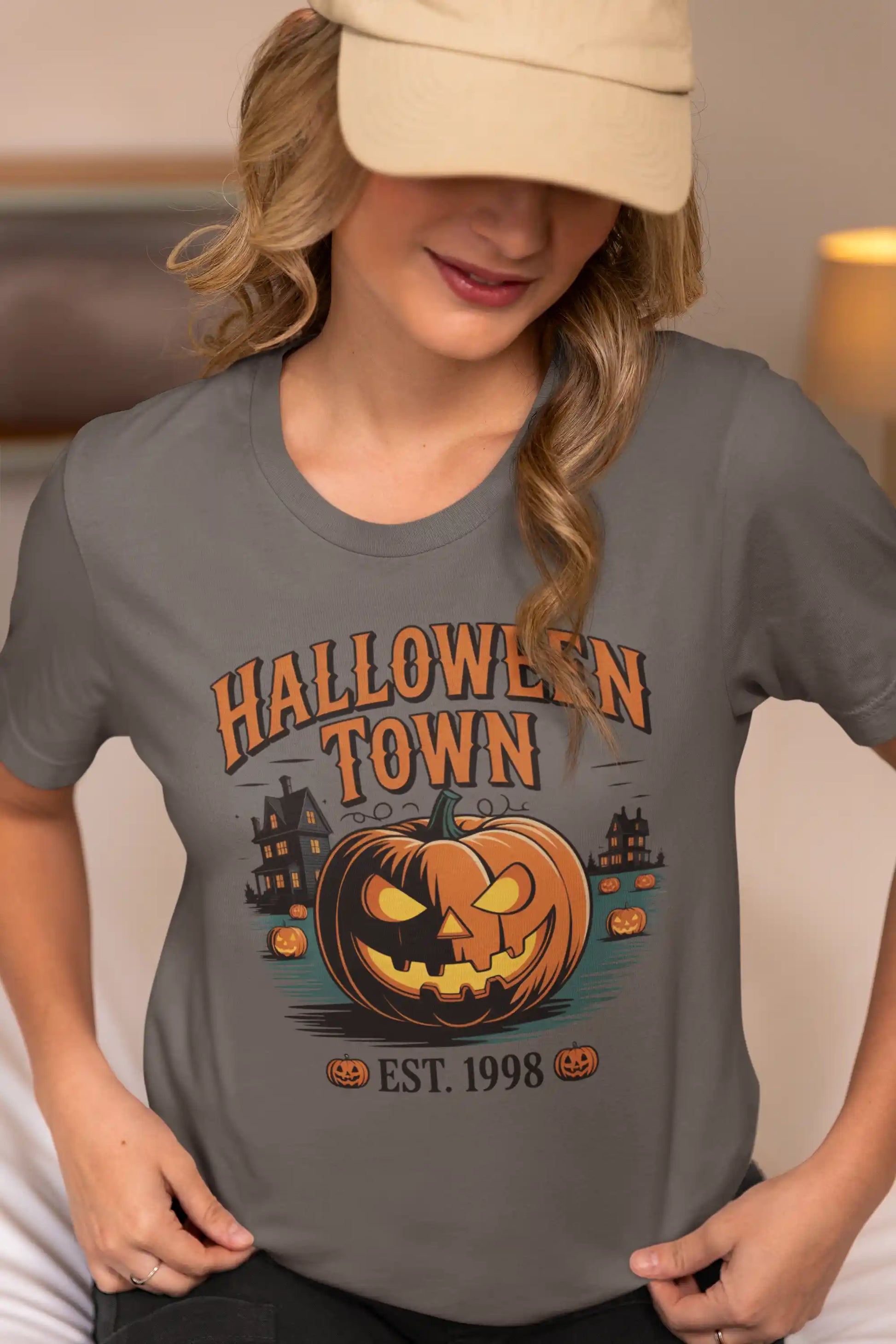 A woman in a baseball cap wears a gray Halloween Town t-shirt with a pumpkin graphic.