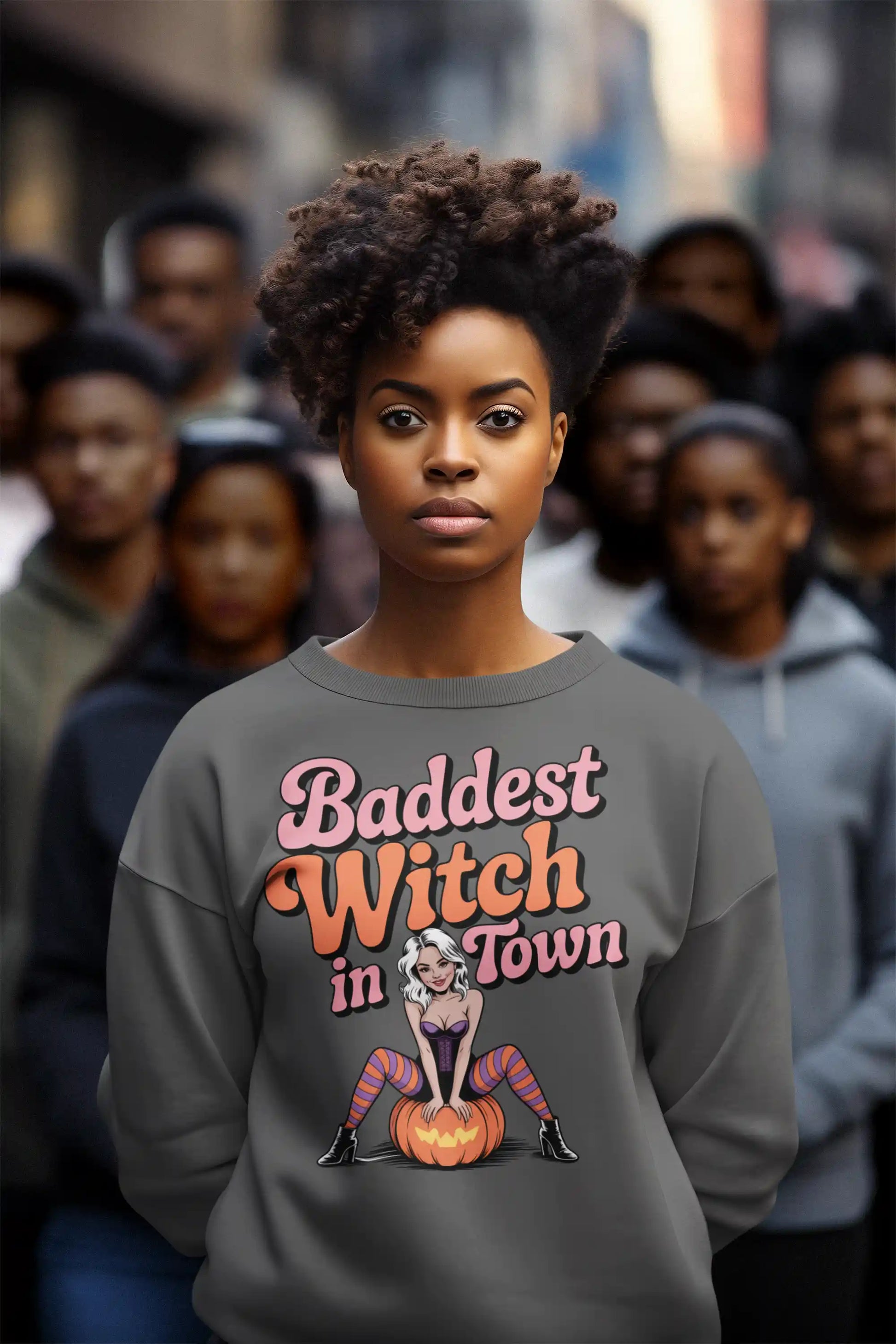 A woman wears a dark gray sweatshirt with "Baddest Witch in Town" and a witch on a pumpkin.