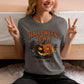A woman in a gray Halloween Town t-shirt with a pumpkin graphic makes peace signs.