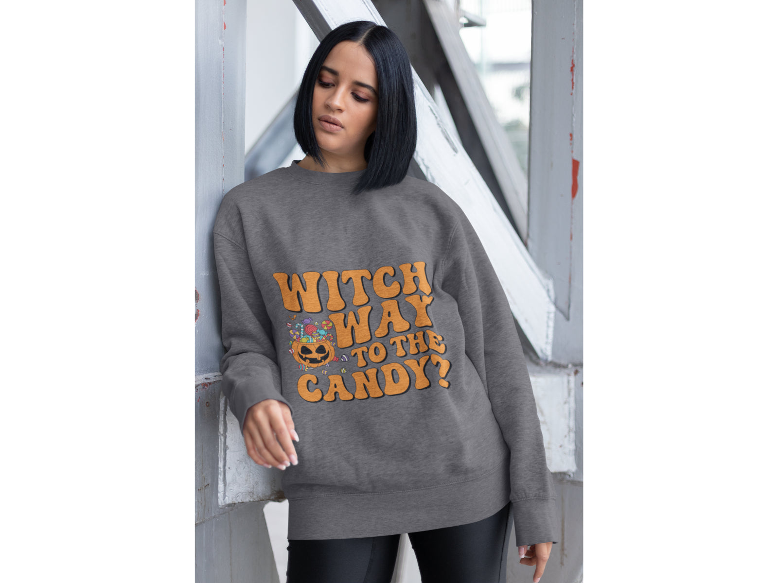 A woman wears a dark gray sweatshirt with "Witch Way to the Candy?" text.