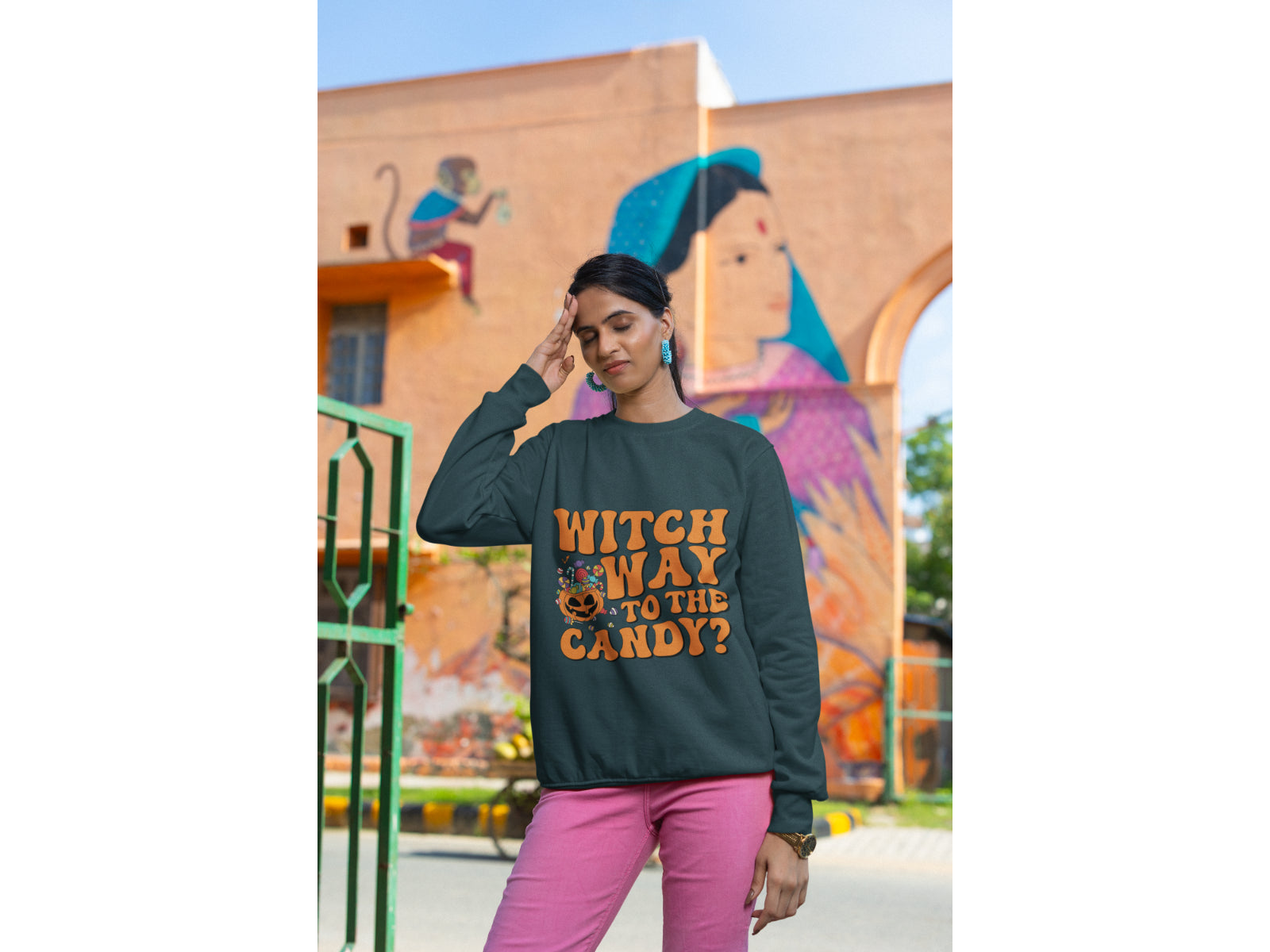 A woman wears a dark green "Witch Way to the Candy?" Halloween sweatshirt.