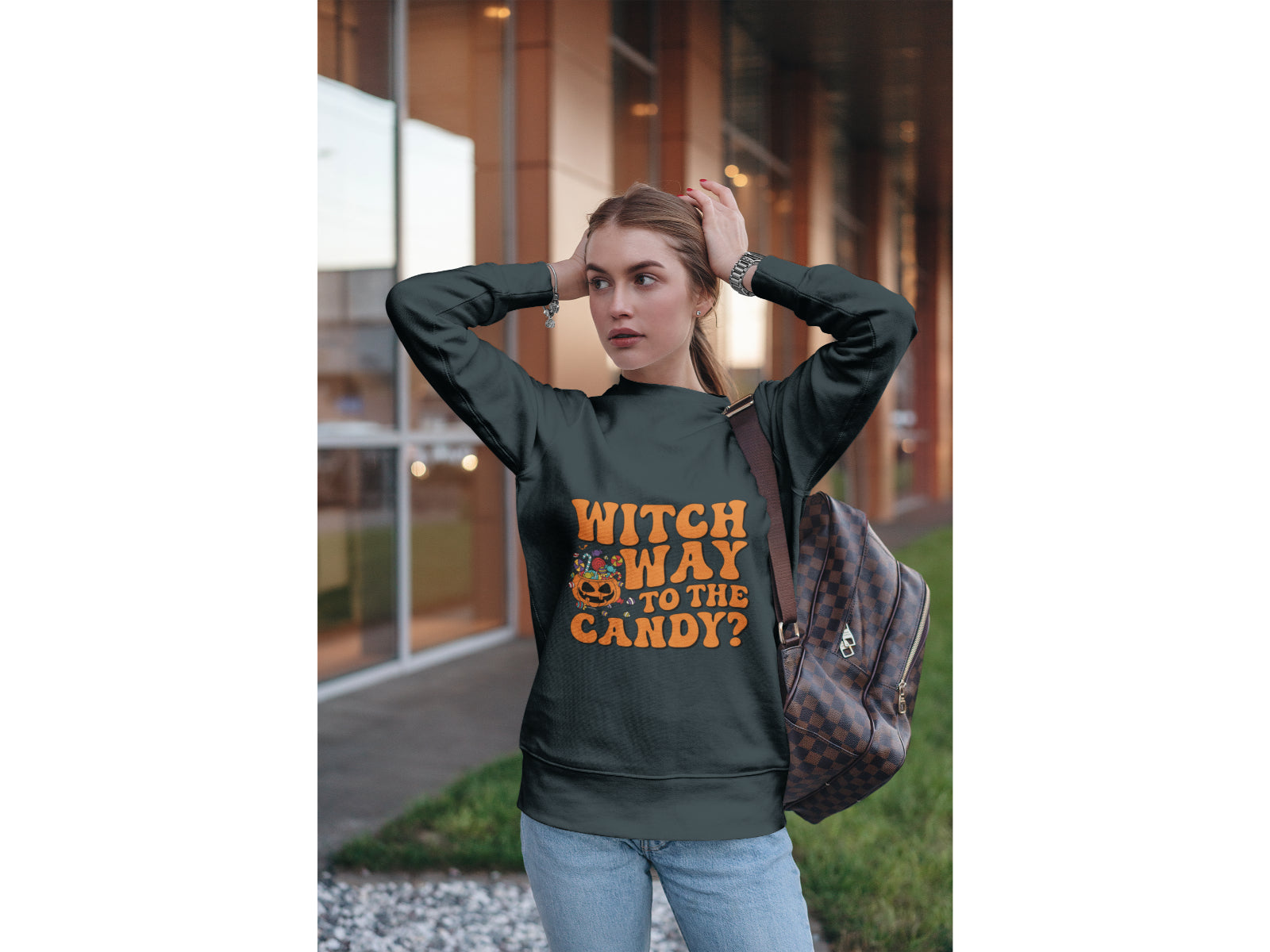 A woman wears a dark grey sweatshirt with "Witch Way to the Candy?" in orange text.
