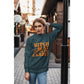 A woman wears a dark green sweatshirt with "Witch Way to the Candy?" in orange text.