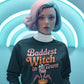 A woman with light hair wears a dark sweatshirt with "Baddest Witch in Town" text.