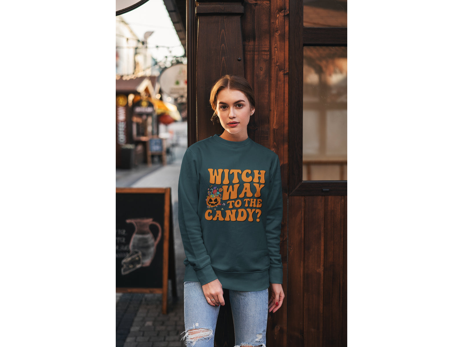 A woman wears a dark green "Witch Way to the Candy?" Halloween sweatshirt.