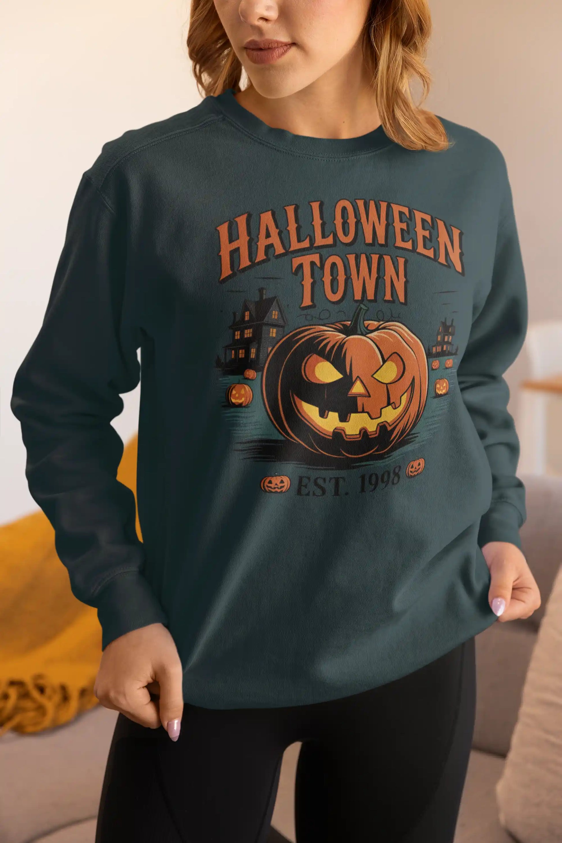 A woman wears a dark green Halloween Town sweatshirt with a pumpkin graphic.