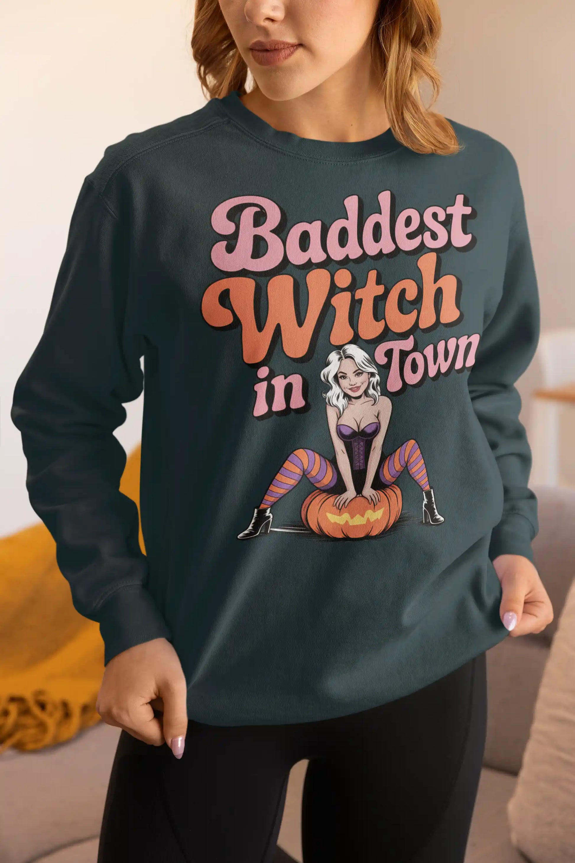 A woman wears a dark green sweatshirt with "Baddest Witch in Town" and a witch graphic.