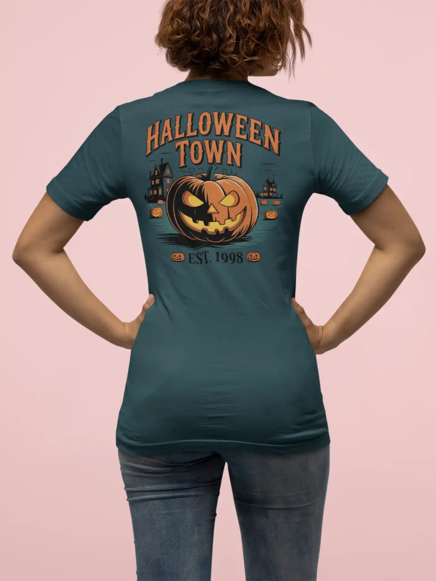A woman from behind wears a dark teal Halloween Town t-shirt with a pumpkin graphic.