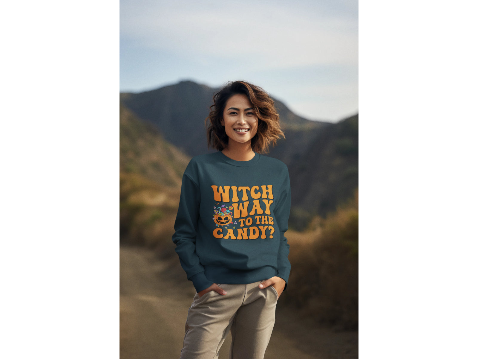 A woman smiles wearing a dark teal "Witch Way to the Candy?" Halloween sweatshirt.