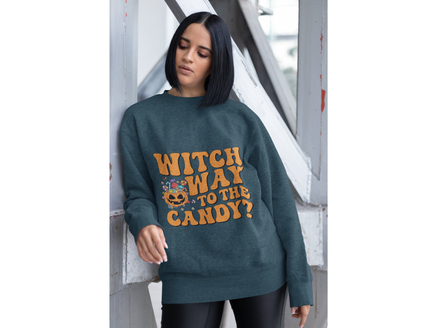 A woman wears a dark teal sweatshirt with "Witch Way to the Candy?" in orange text.