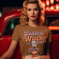 A woman wears a brown t-shirt with "Baddest Witch in Town" and a witch graphic.