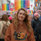 A woman wears a brown Halloween Town hoodie with a pumpkin graphic.