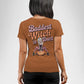 A woman from behind wears a brown t-shirt with "Baddest Witch in Town" and a witch graphic.