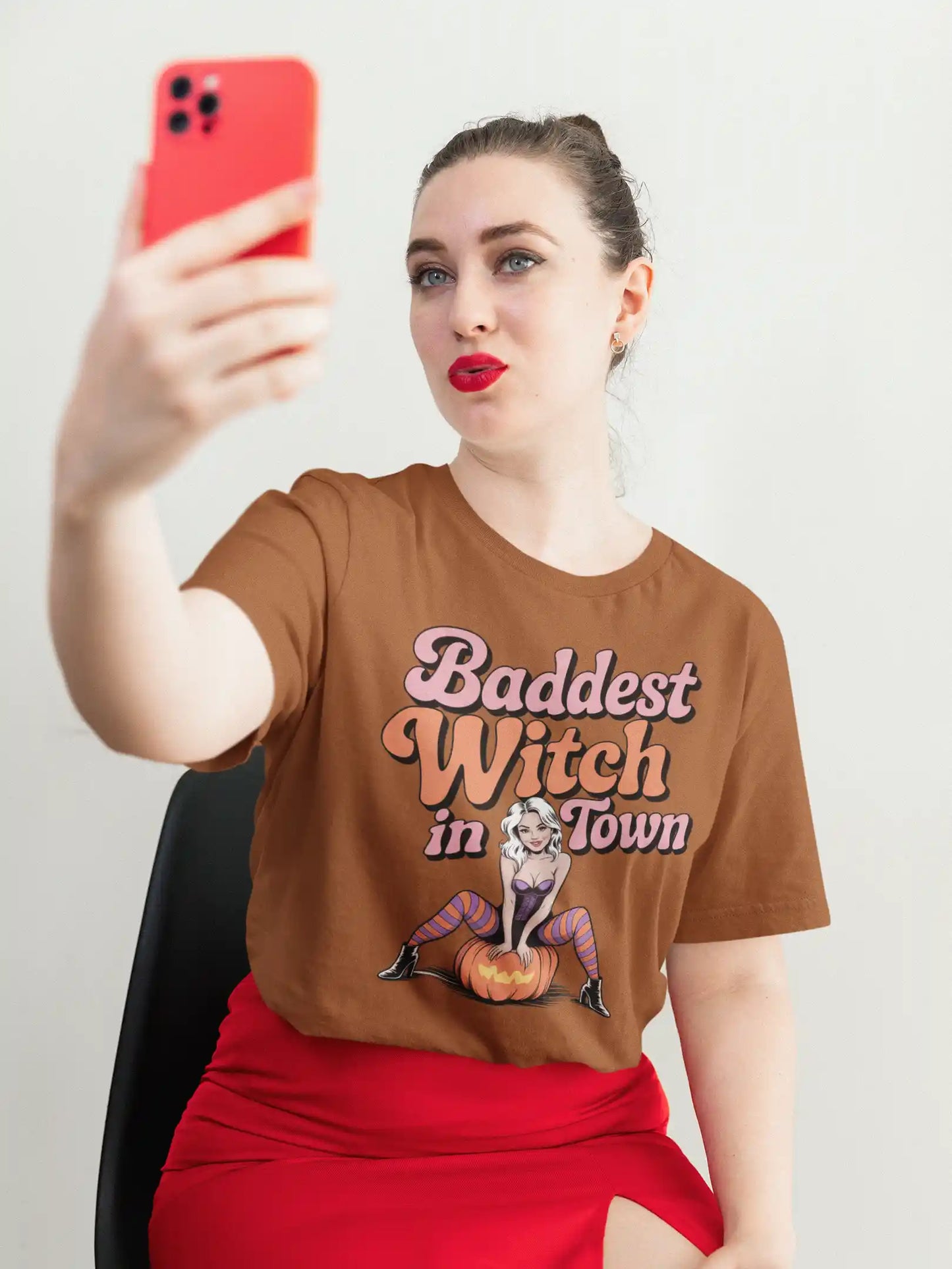 A woman in a brown "Baddest Witch in Town" t-shirt takes a selfie.