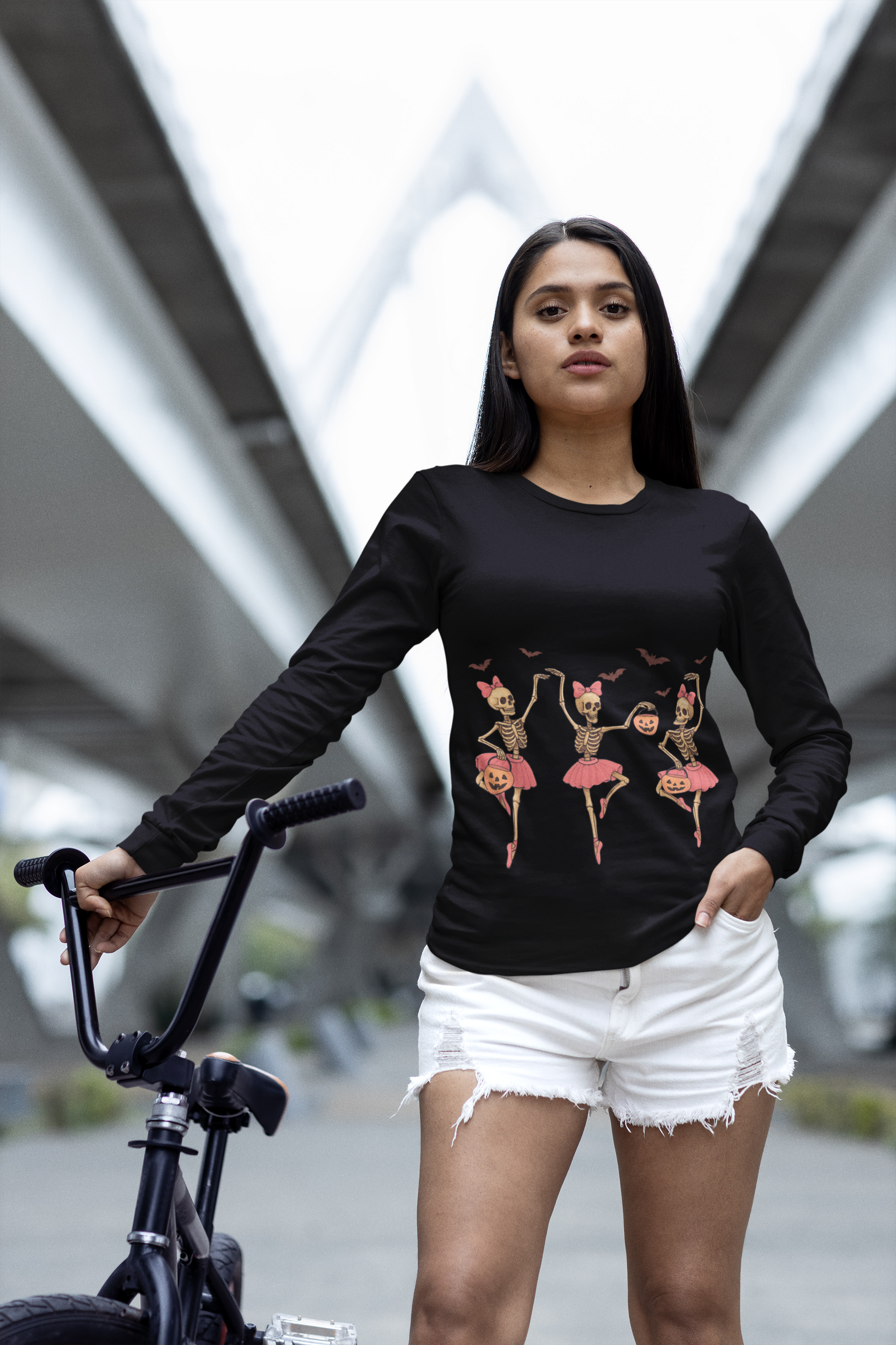 A woman in a black long-sleeve shirt with dancing skeleton ballerinas holds a bike.