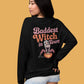 A woman models a black sweatshirt with "Baddest Witch in Town" and a witch graphic.