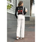 A woman wears a black long-sleeve shirt with a red skull cherry design and white pants.