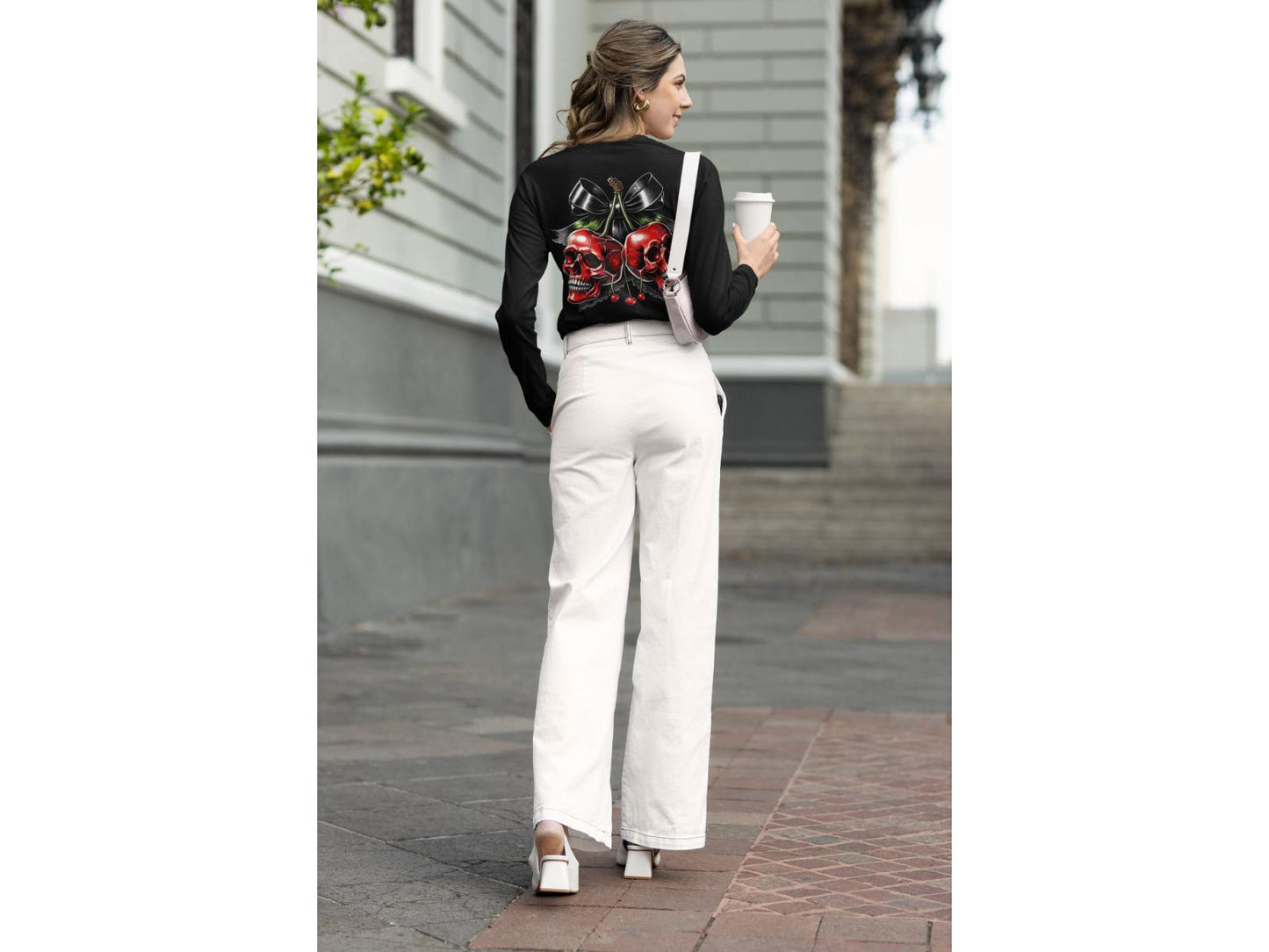 A woman wears a black long-sleeve shirt with a red skull cherry design and white pants.