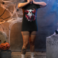 A woman in a black t-shirt with a creepy ghost design stands in a Halloween setting.