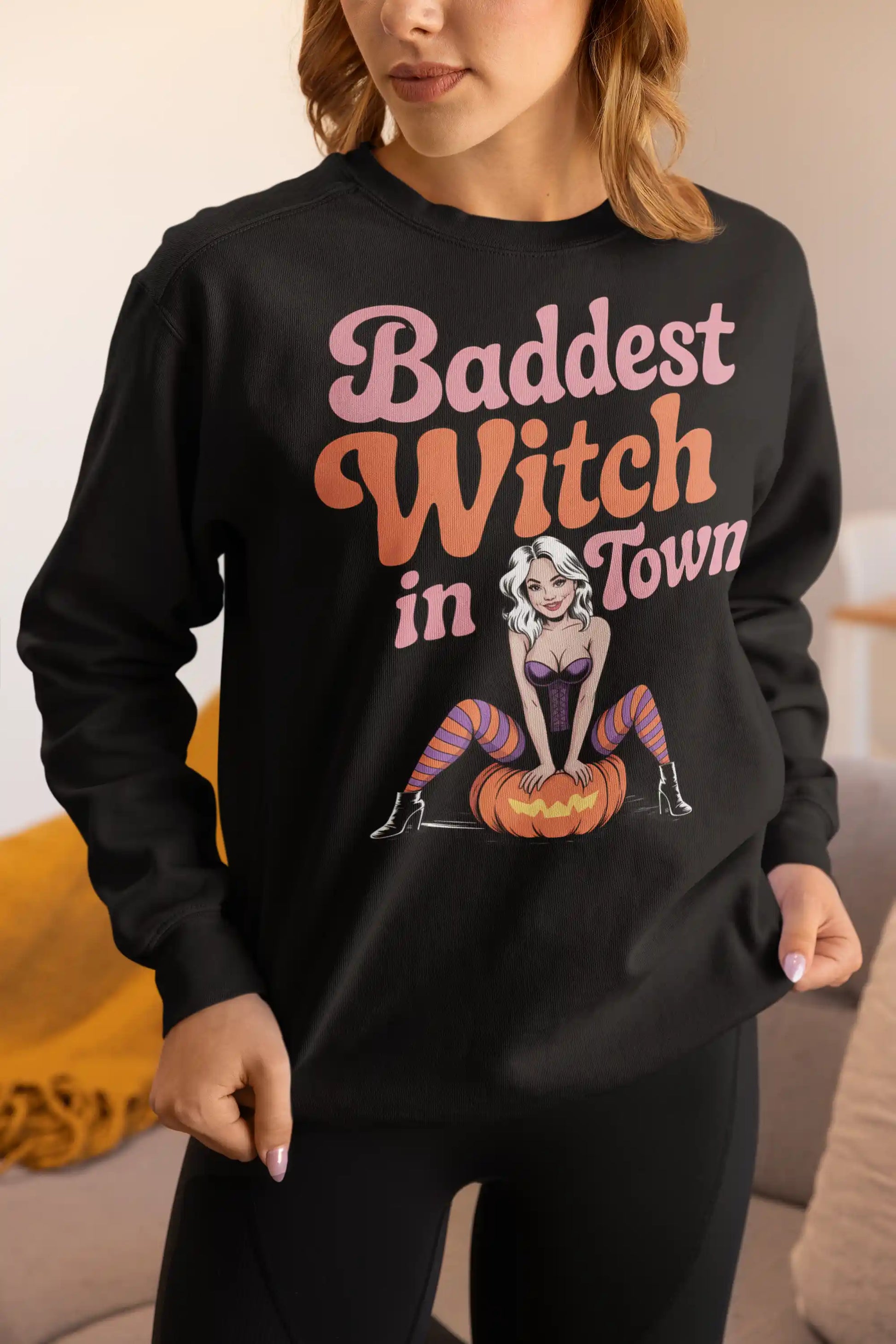 A woman wears a black sweatshirt with "Baddest Witch in Town" and a witch on a pumpkin.