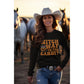 A woman in a black "Witch Way to the Candy" Halloween sweatshirt stands with horses.
