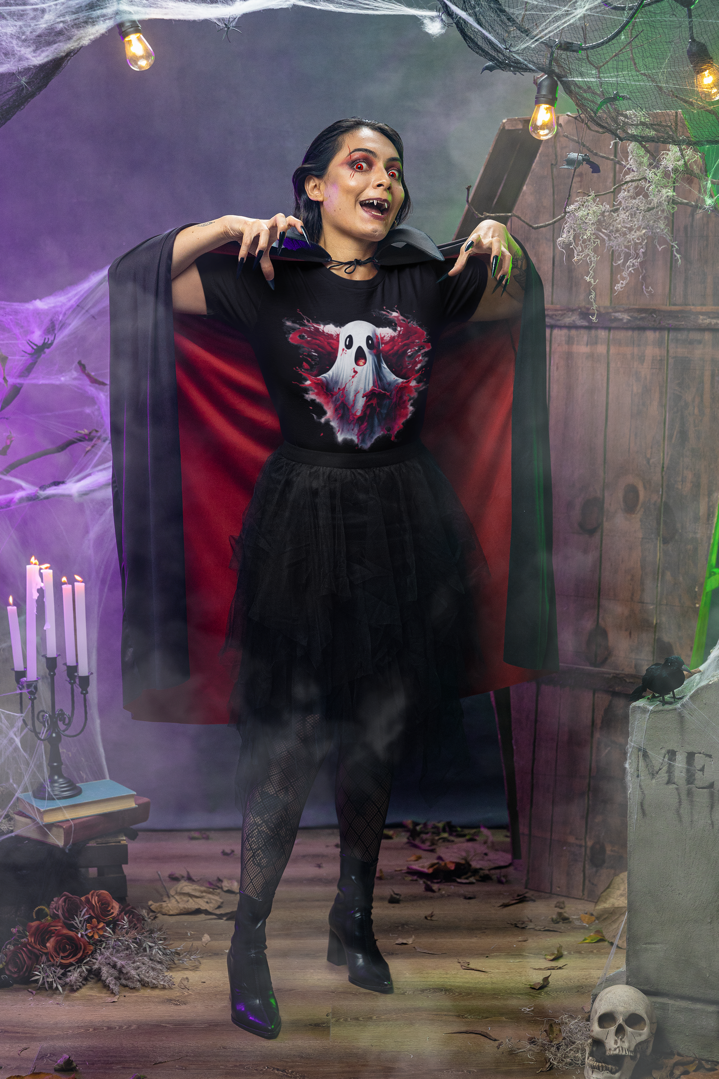 A woman in a ghost t-shirt, black skirt, and cape poses in a Halloween setting.