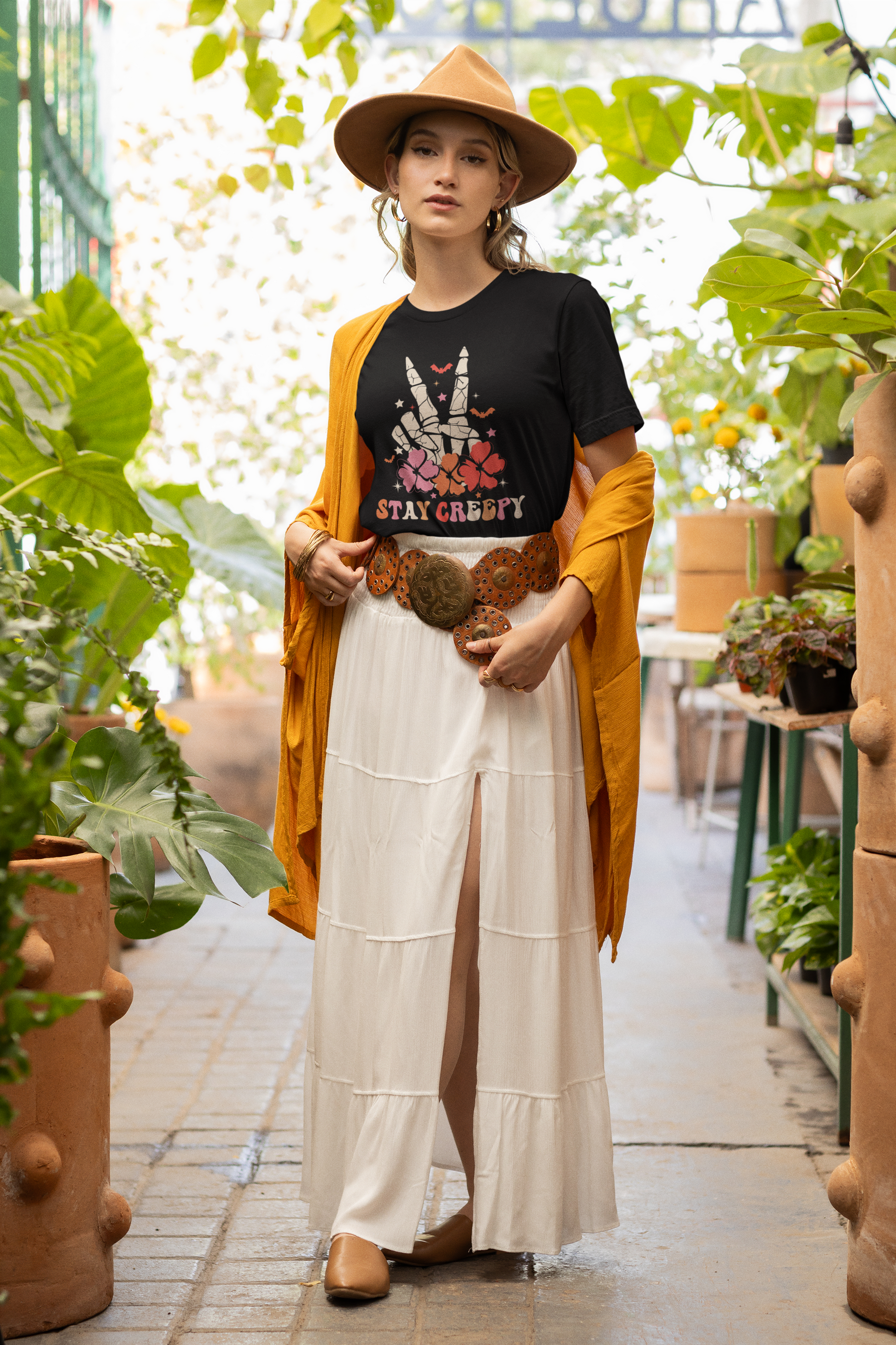 A woman wears a black t-shirt with a "Stay Creepy" graphic and a brown hat.