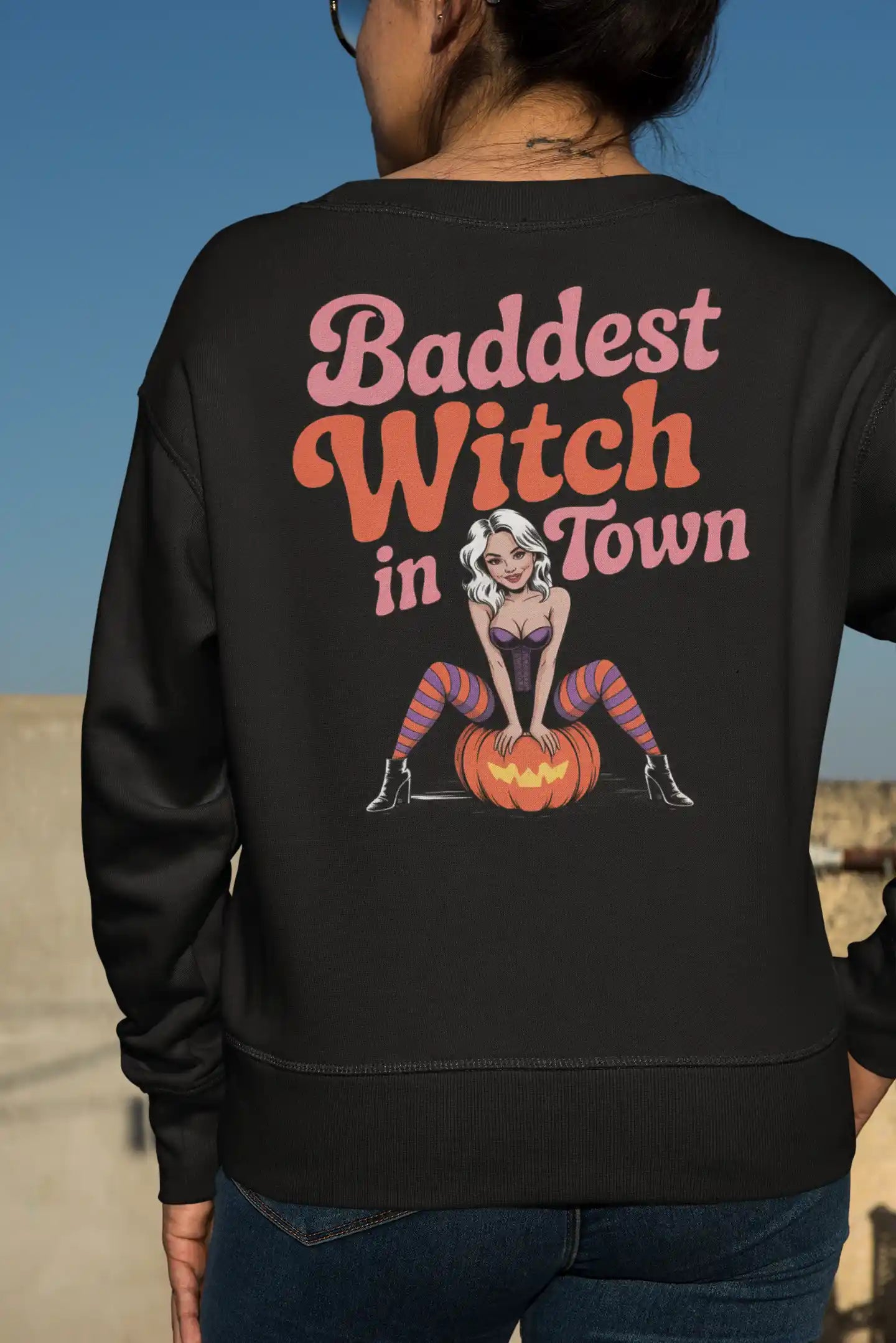 A person from behind wears a black sweatshirt with "Baddest Witch in Town" text.