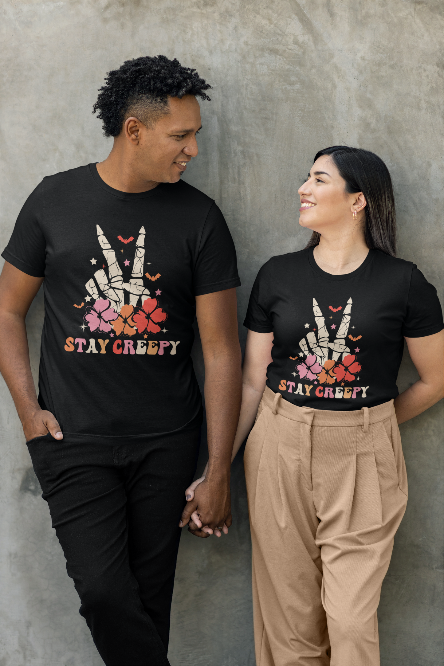 A couple wears black t-shirts with a skeleton hand peace sign and "Stay Creepy" text.