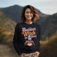 A woman in a black "Baddest Witch in Town" sweatshirt stands outdoors.