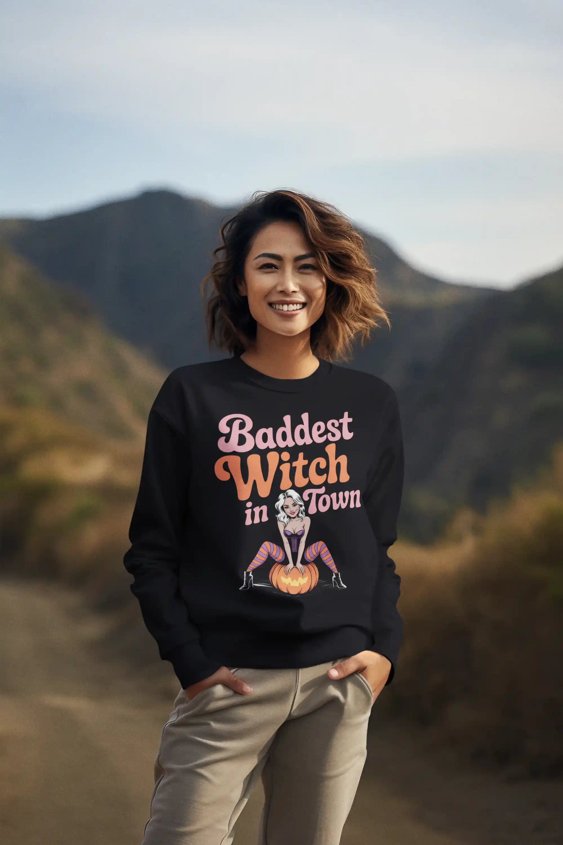 A woman in a black "Baddest Witch in Town" sweatshirt stands outdoors.