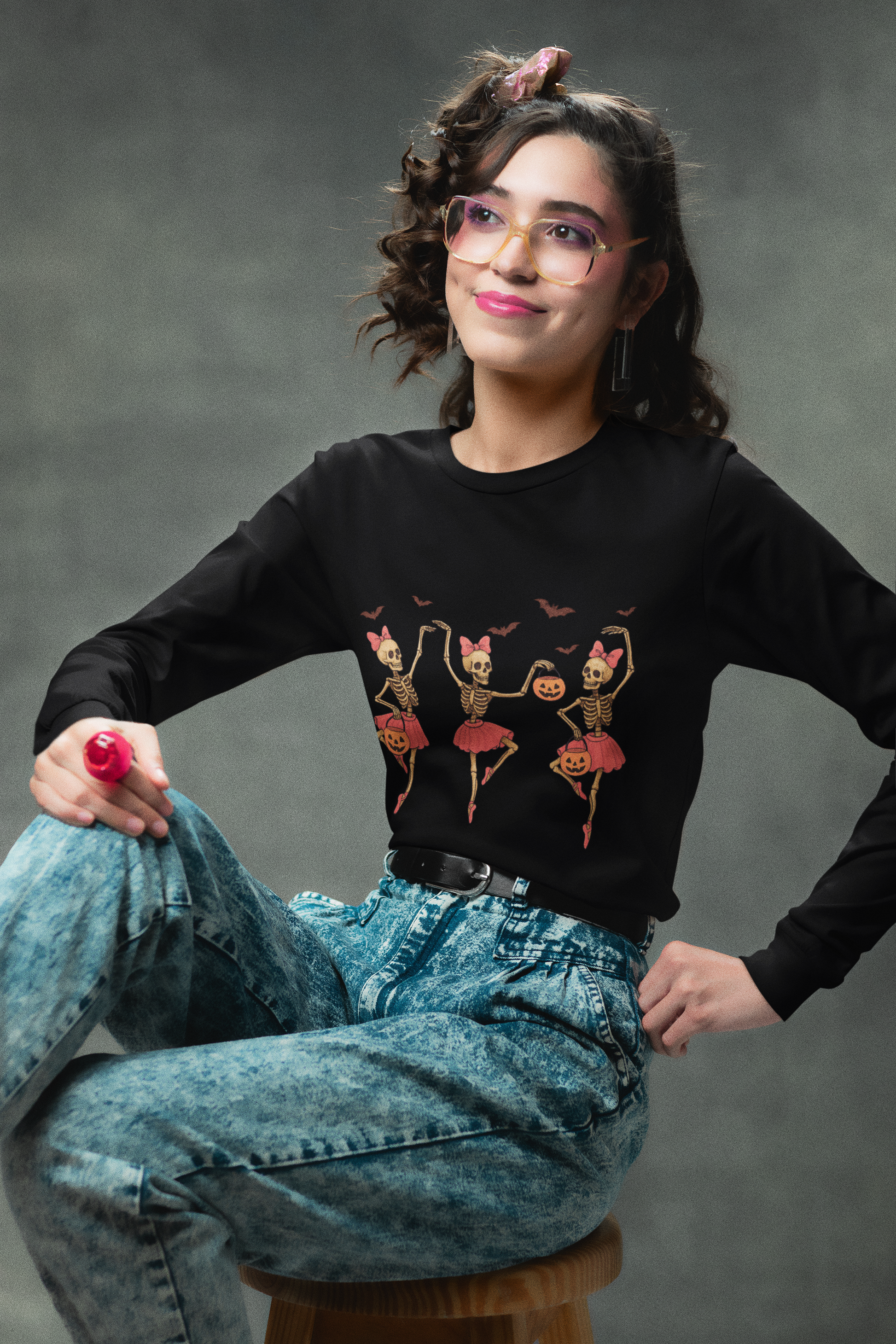 A woman wears a black long-sleeve shirt with dancing skeleton ballerinas and acid-wash jeans.