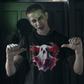 A person with zombie makeup points to a black t-shirt with a creepy ghost design.