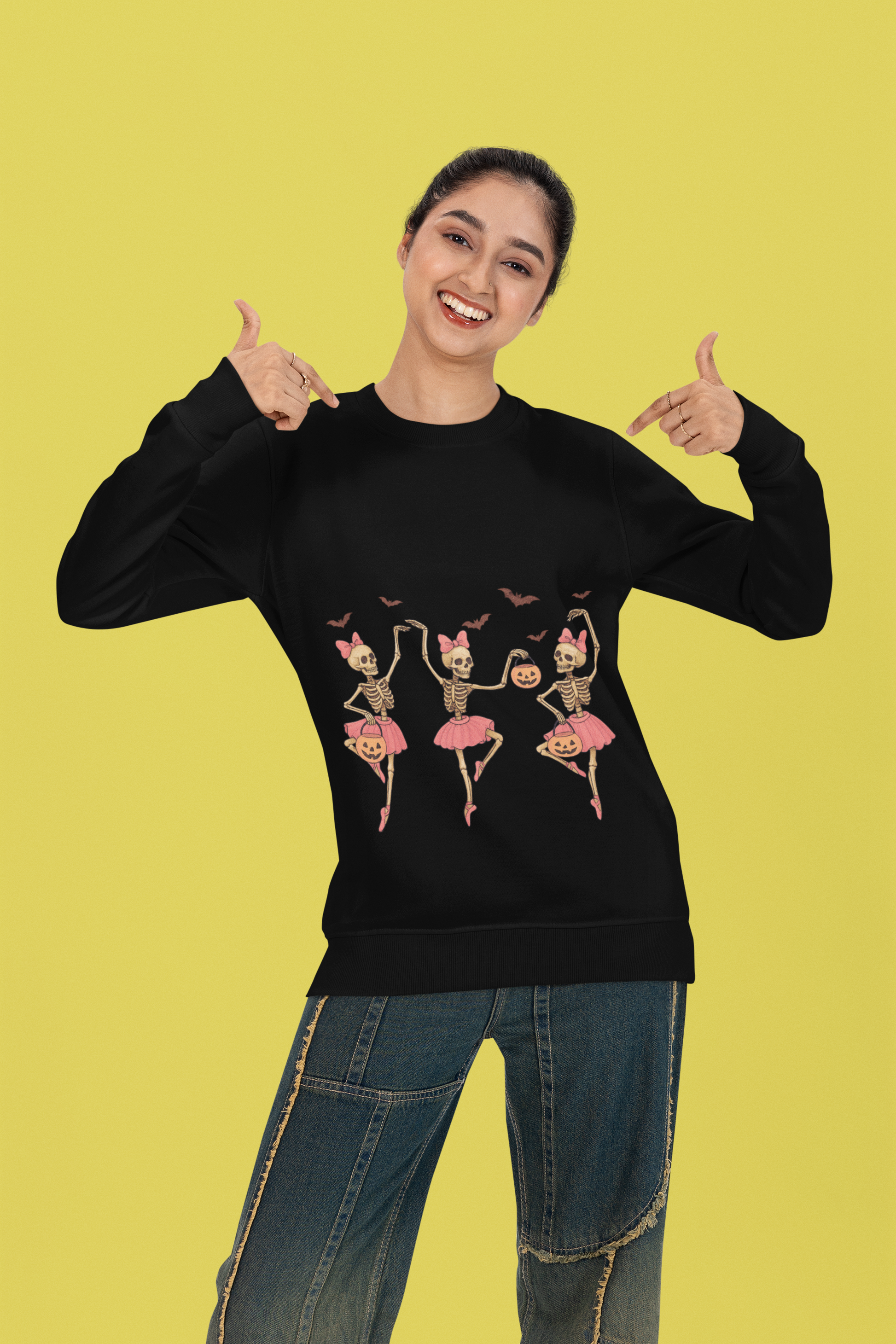 A woman smiles, pointing to her black long-sleeve shirt with dancing skeleton ballerinas.