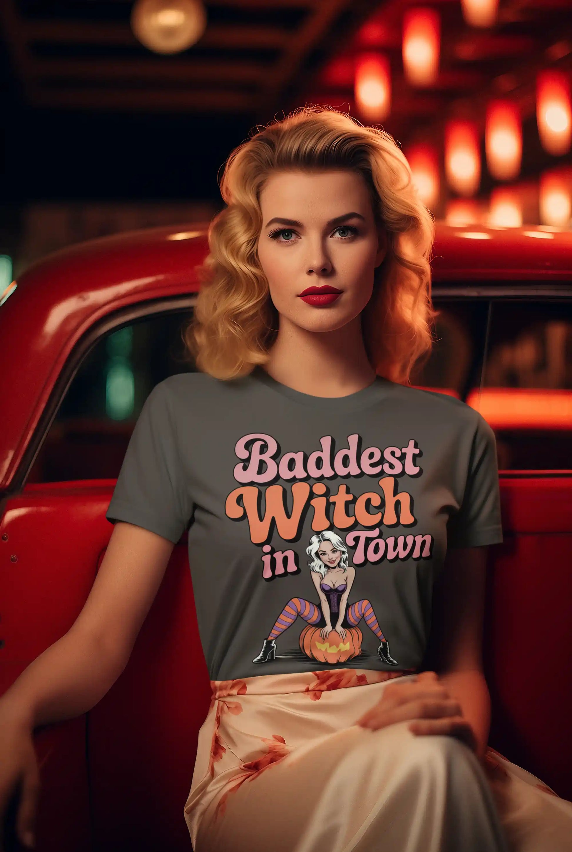 A woman in a gray "Baddest Witch in Town" t-shirt sits in a red car.