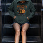 A person wearing a dark green Halloween Town hoodie with a pumpkin graphic sits on metal stairs.