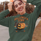 A woman smiles, wearing a dark green Halloween Town hoodie with a pumpkin graphic.