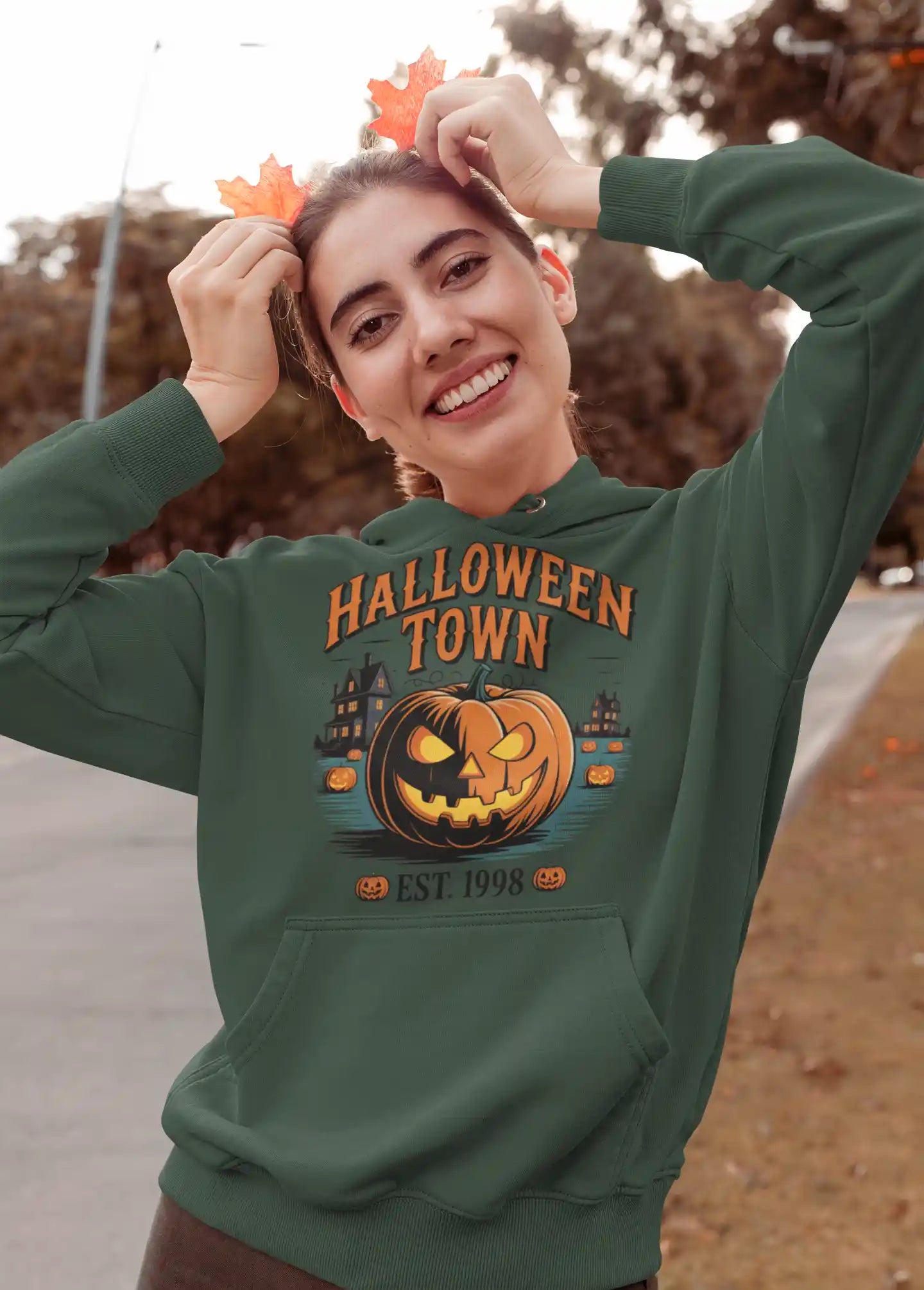 A woman smiles, wearing a dark green Halloween Town hoodie with a pumpkin graphic.