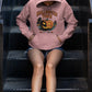 A person wearing a pink Halloween Town hoodie with a pumpkin graphic sits on metal stairs.