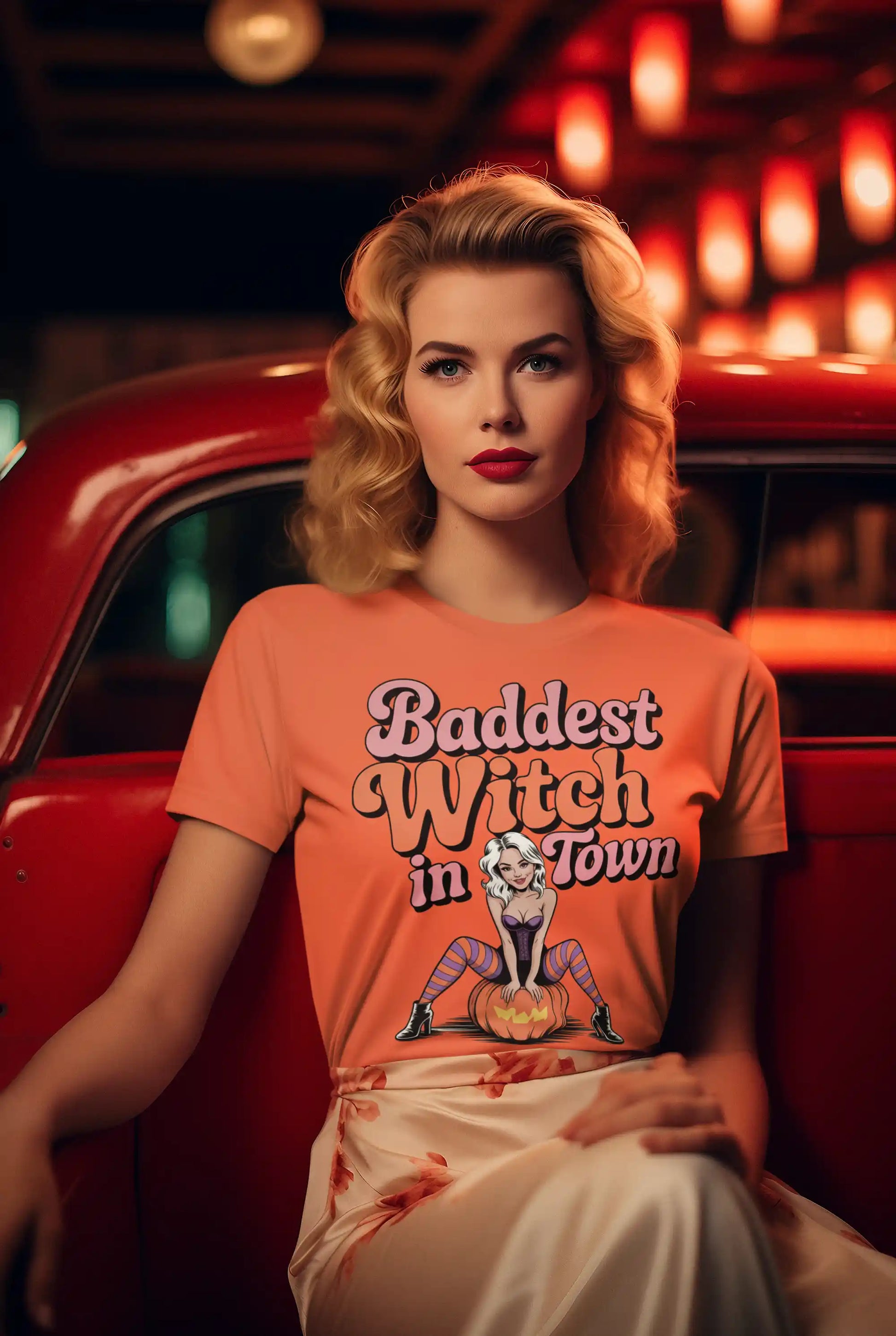 A woman with blonde hair and red lipstick wears an orange "Baddest Witch in Town" t-shirt.