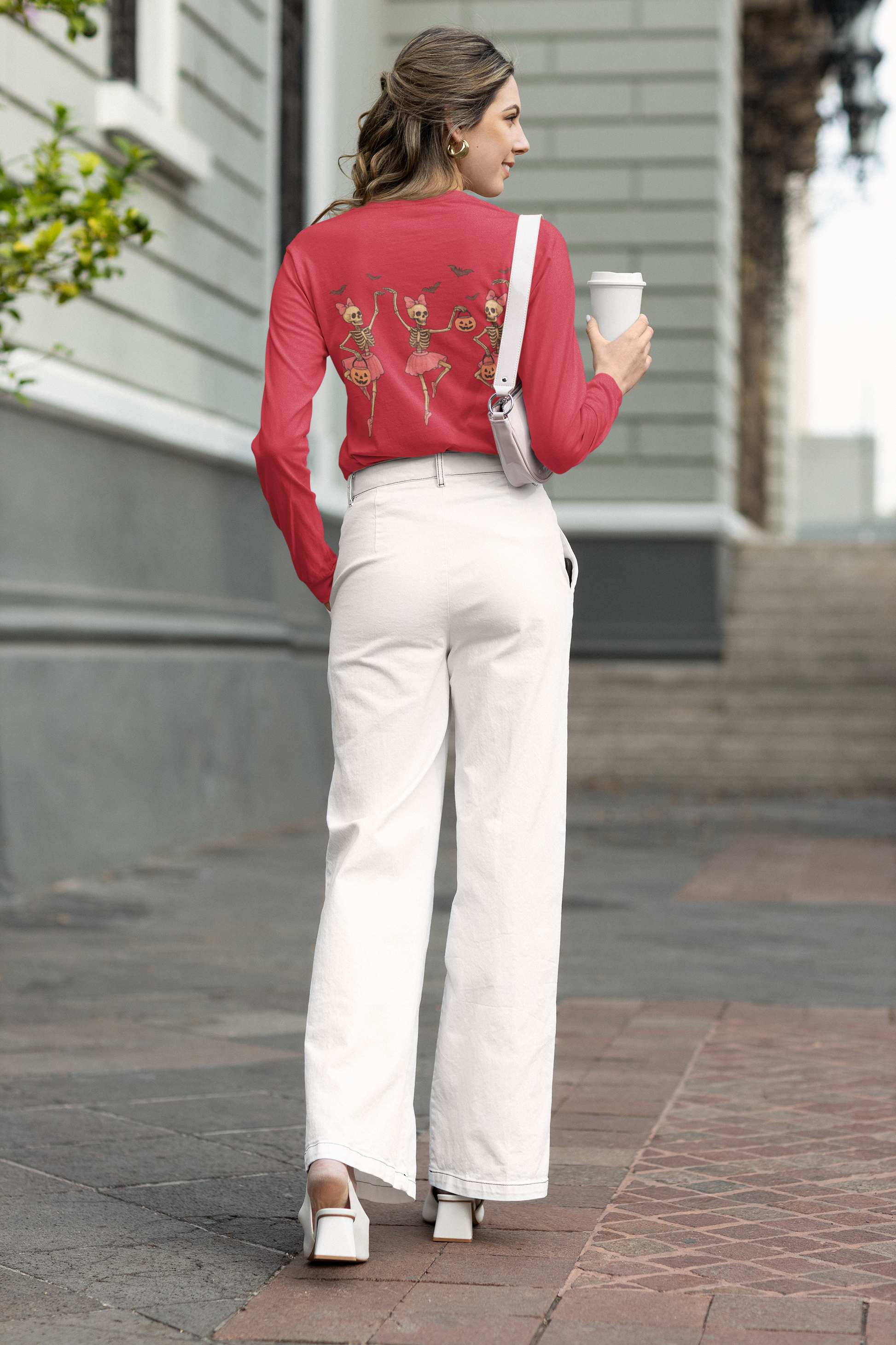 A woman wears a red long-sleeve shirt with dancing skeleton ballerinas on the back.