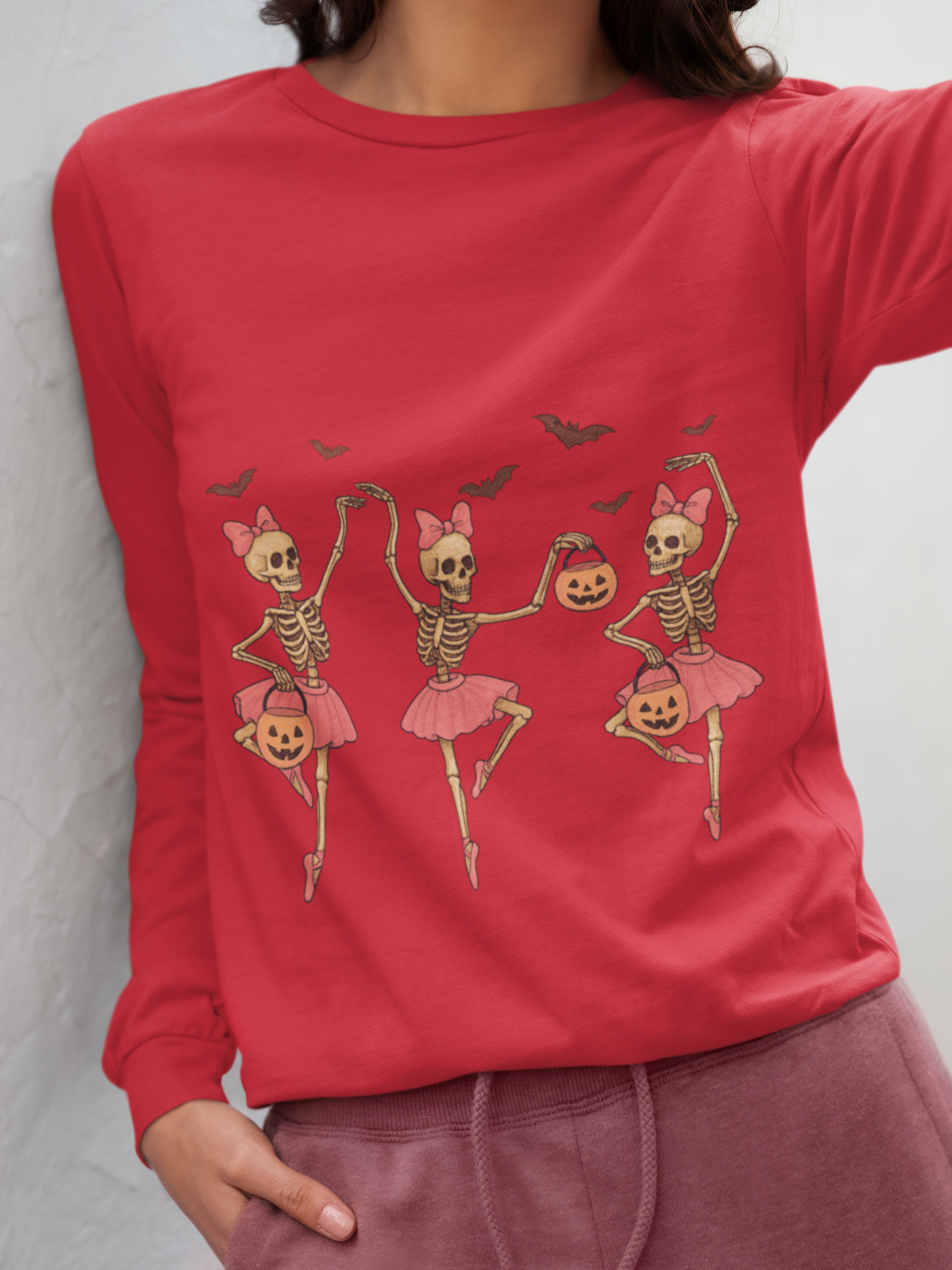 A woman wears a red long-sleeve shirt with three dancing skeleton ballerinas.