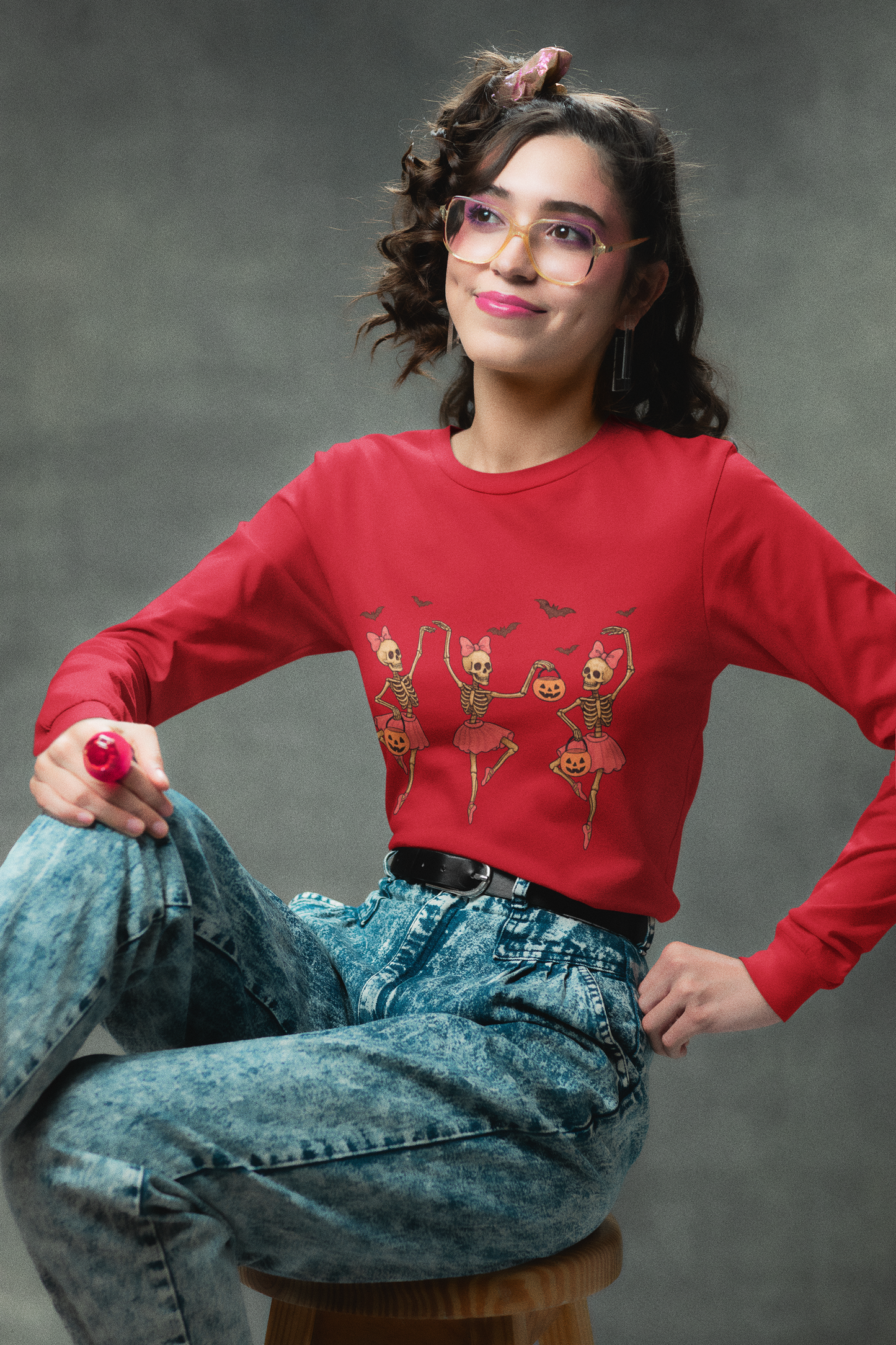 A woman in a red long-sleeve shirt with dancing skeleton ballerinas and acid-wash jeans.