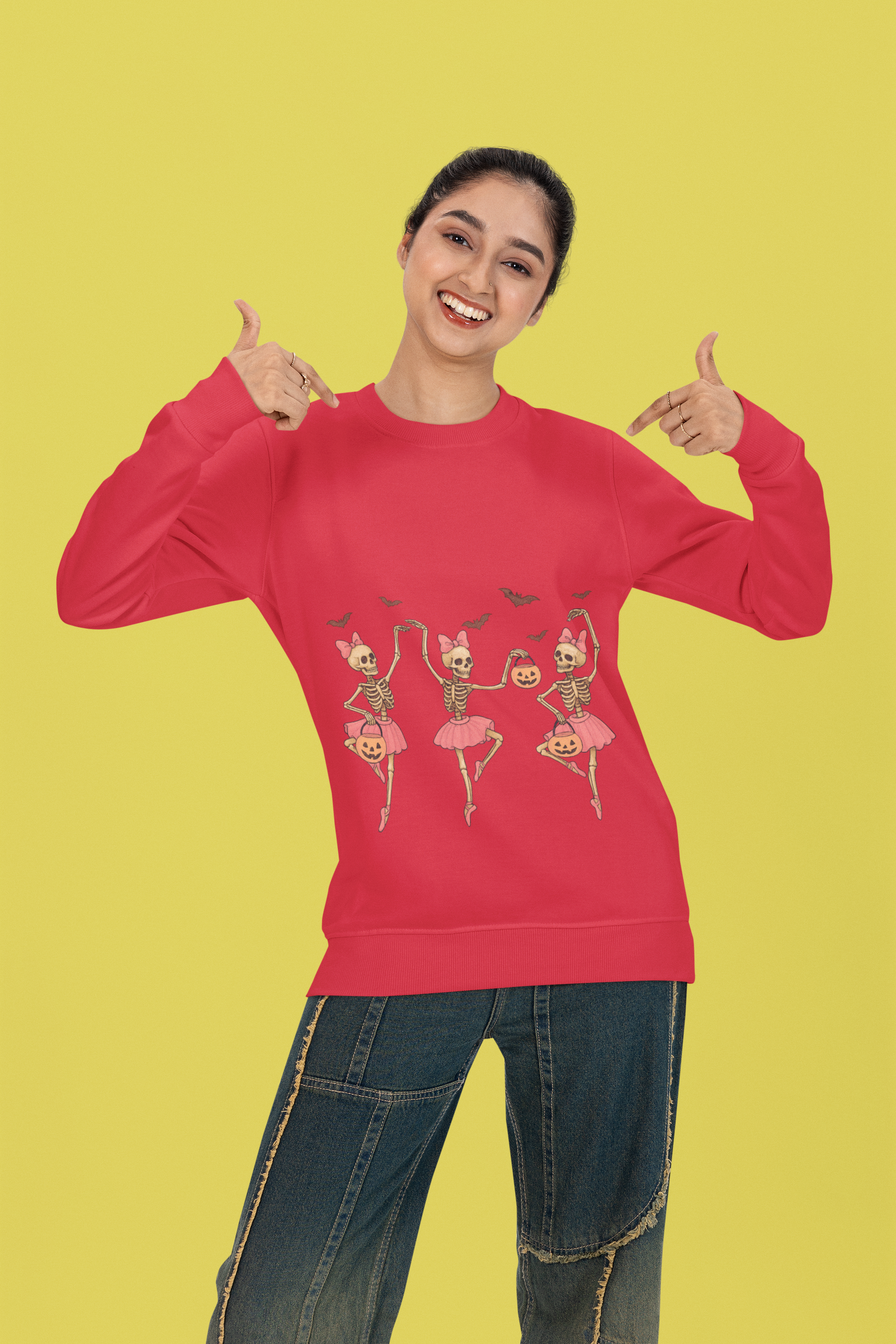 A woman in a red long-sleeve shirt with dancing skeleton ballerinas points to her shirt.