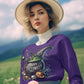 A woman in a purple Halloween sweatshirt and a straw hat holds pink flowers.