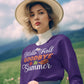 A woman in a purple "Hello Fall Goodbye Summer" sweatshirt holds pink flowers.