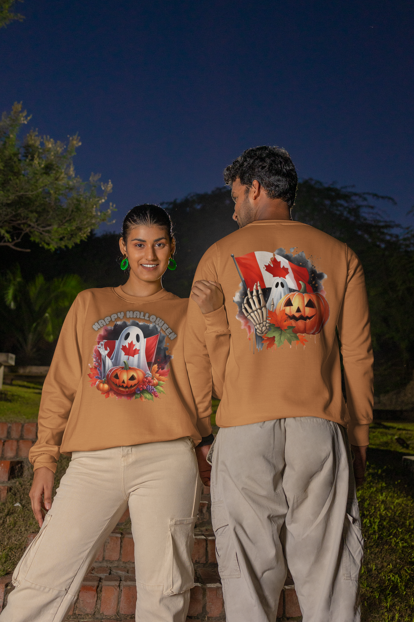Two people wear matching tan long-sleeve Halloween-themed sweatshirts with Canadian flag designs.