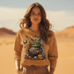 A woman in a desert wears a long-sleeve sweatshirt with a Halloween cauldron design.